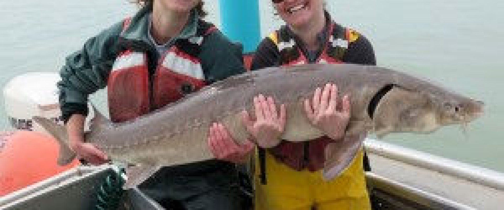 Two biologists stand on a boat and hold a Lake Sturgeon together. 
