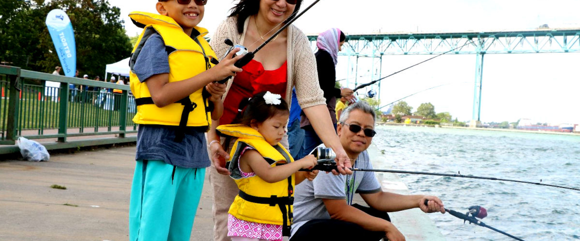 A family fishes in the Detroit River with the Ambassador Bridge in the background. 
