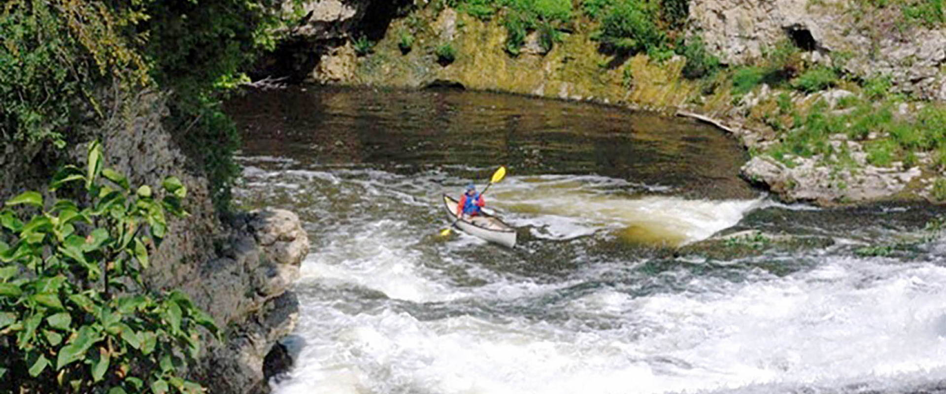 A man paddles by cliffs and into rapids on the Grand River