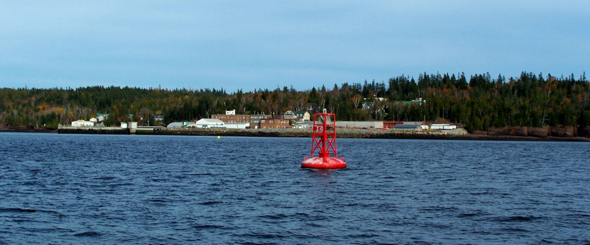 Blue skies and water with a biological station on the far shore. There is a red bell buoy in the foreground. 