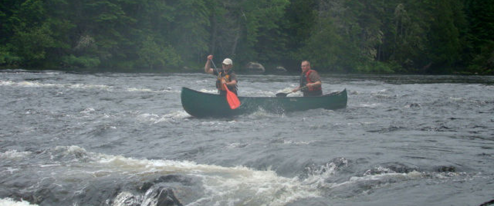 Two people in a green canoe paddle through the misty Canoose Ledges towards the rapids of the St. Croix River. 