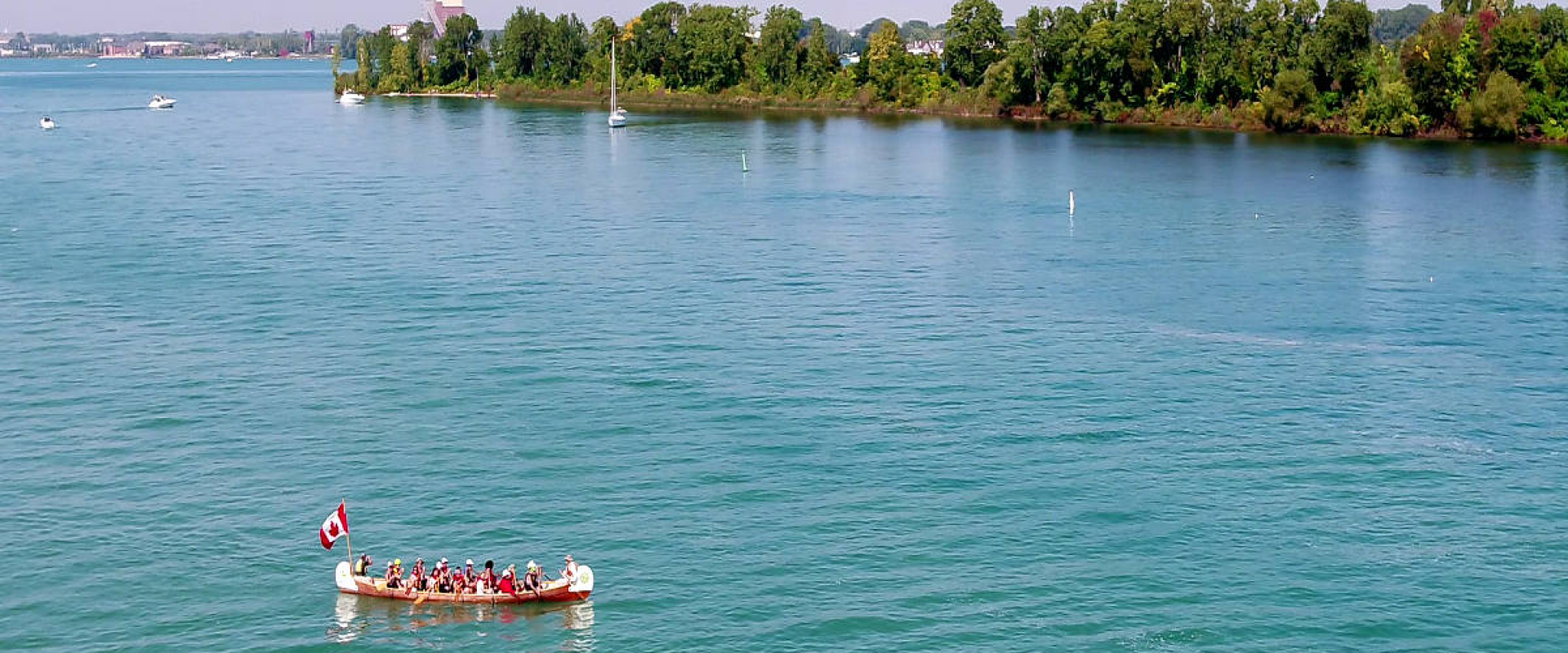 A voyageur canoe carries paddlers across the Detroit River in the foreground of Peche Island on a clear day.