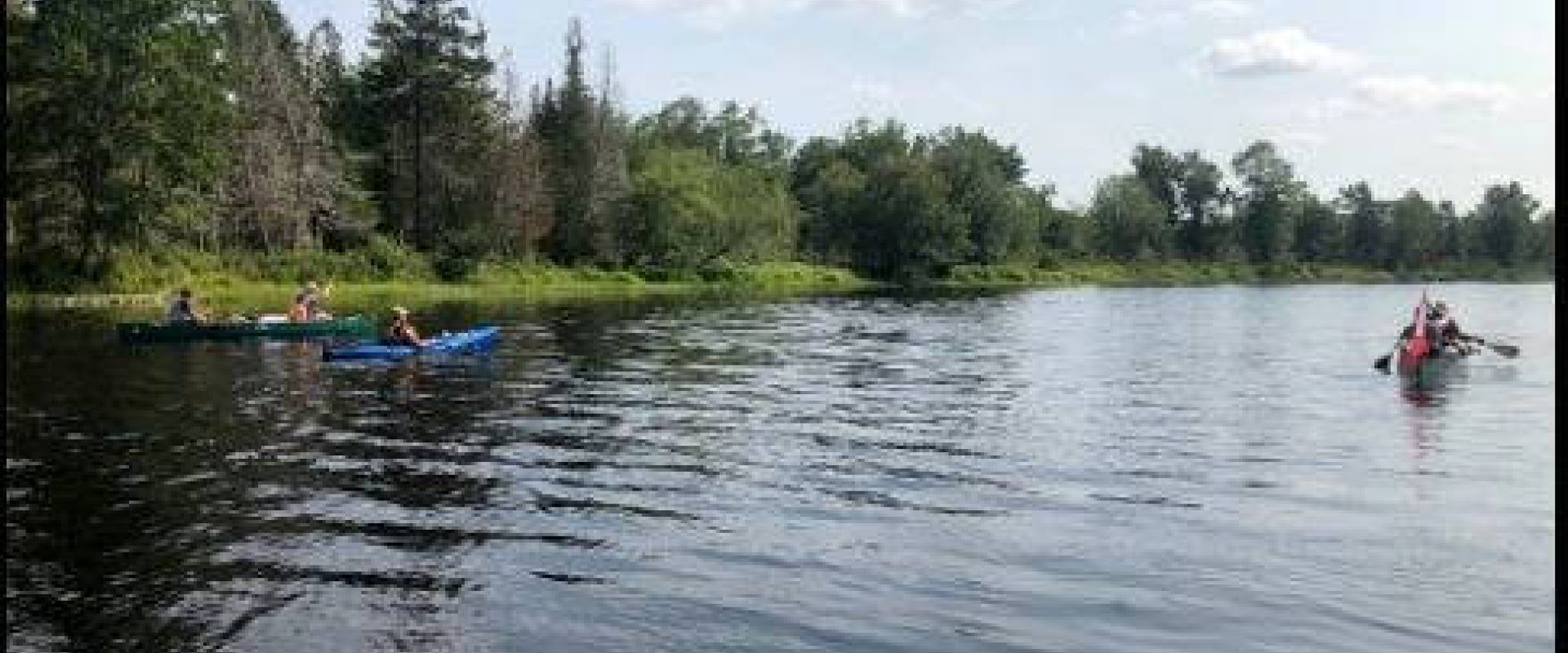 Canoers and kayakers paddle calm waters of the St. Croix River with green trees along the far shore.