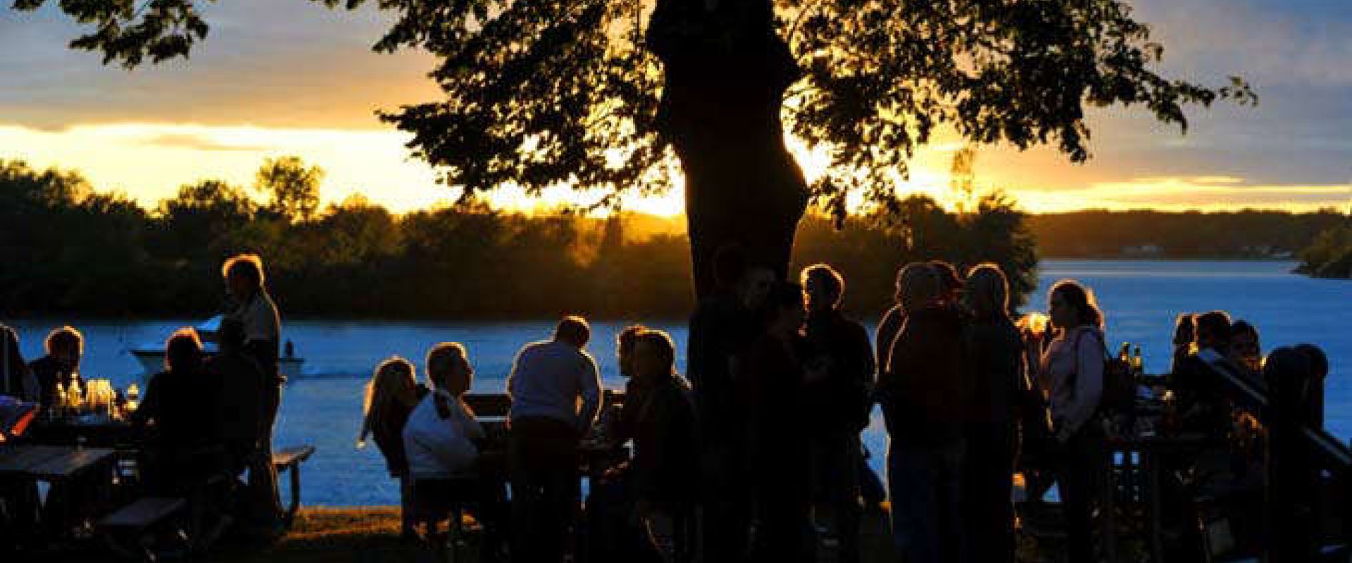 People gather around picnic tables at sunset on the shore of Lake Erie during the annual Lake Erie Wine Festival. 