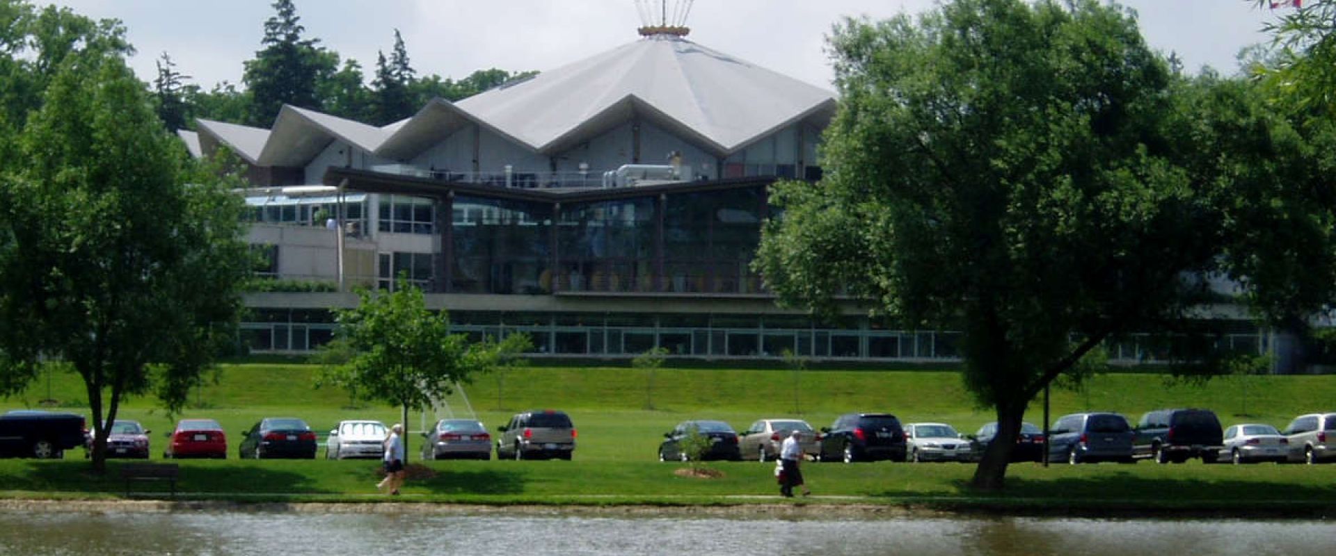 The Stratford Festival Theatre is located along the Thames River. It is a large, round theatre building with a fluted roof and flag on top. 