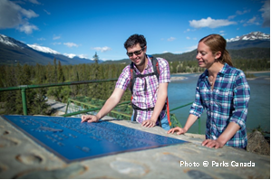 Des visiteurs lisent la plaque commémorative de la rivière du patrimoine Photo © Parks Canada canadien Athabasca dans le parc national Jasper, en Alberta.