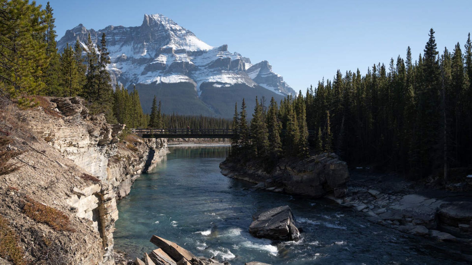 A bridge crossing the North Saskatchewan River with a snow-covered mountain in the background.