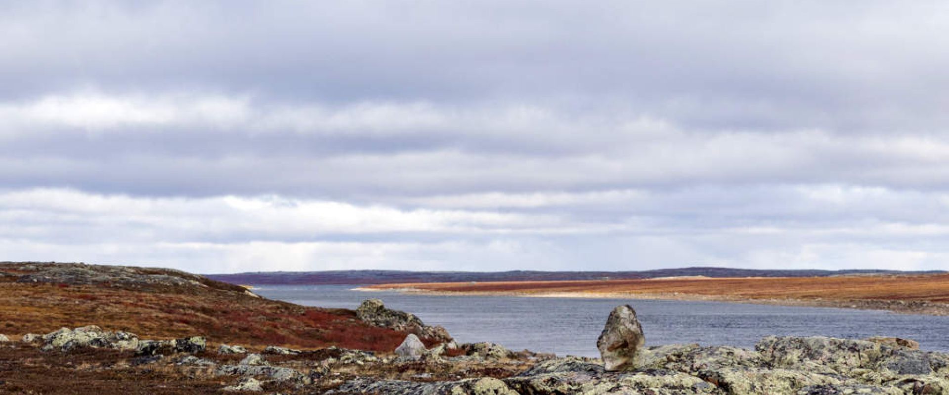 A rocky outcrop is dotted by a large stone propped upright. This is a way marker for past and present Inuit.